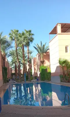 a swimming pool with palm trees and a building at Riyad Entier Avec piscine Red Moon Kech in Marrakech