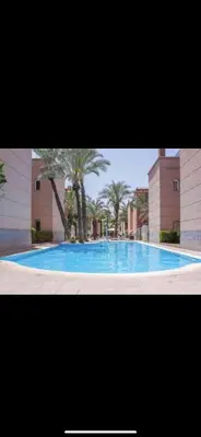 a large blue swimming pool with palm trees and buildings at Dxb Riad 4 suites in Marrakech