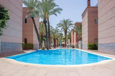 a large blue swimming pool in a building with palm trees at Riad à Marrakech dans la Résidence Touristique Al Qaria Assiyahia in Marrakech