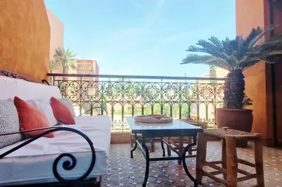 a balcony with a couch and a table and a palm tree at Appartement raffiné idéalement situé avec piscine in Marrakech