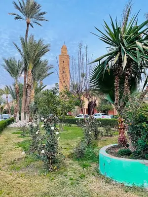 a building with a clock tower in a park with palm trees at Riad Majestic Marrakech in Marrakech
