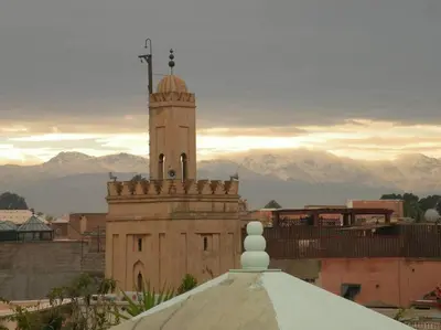 a building with a clock tower with mountains in the background at RIAD PRIVATISÉ 3 Chambres 6 Personnes Place Jemma El Fna in Marrakech