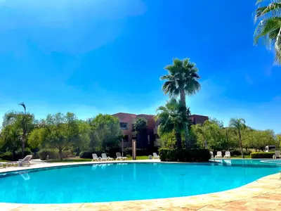 a swimming pool with a palm tree and a building at Luxurious Stay at Prestigia Golf Marrakech with Golf Course, Pool, and Breathtaking Atlas Mountains View in Marrakech