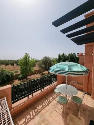 a patio with a table and chairs and an umbrella at Marrakech Atlas Golf Resort appartement 2 chambres,Piscines in Marrakech