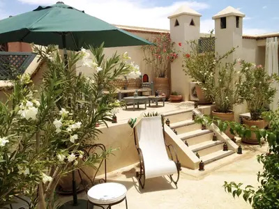 a patio with benches and an umbrella and plants at Riad of The Light in Marrakech