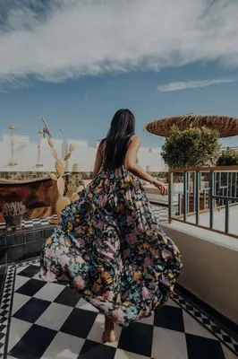 a woman in a floral dress walking on a balcony at Le Petit Kenzara & magical rooftop in Marrakech