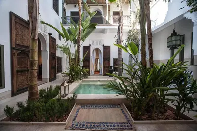 a courtyard with a swimming pool in a building with trees at Riad Jaaneman in Marrakech