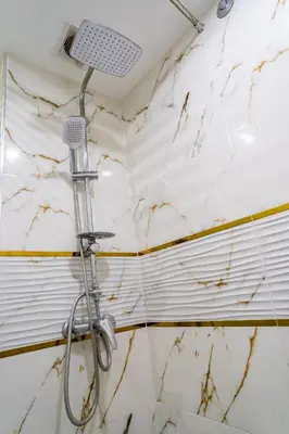 a shower head in a bathroom with a marble wall at L'horizon Aéroport Appartement in Marrakech