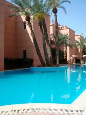 a swimming pool with palm trees in front of a building at Riad QAYS in Marrakech