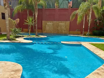 a blue swimming pool with palm trees and a red fence at Résidence Soltana, Marrakech in Marrakech