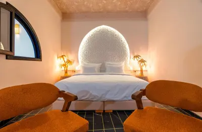 a bedroom with a large white bed with two chairs at Riad L'ECOLE in Marrakech