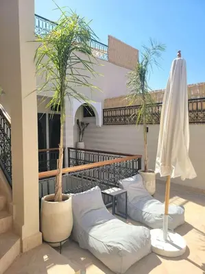 a patio with two chairs and an umbrella and palm trees at Riad Isahiac avec piscine en exclusivité in Marrakech