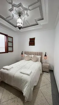 a white bedroom with a large bed and a chandelier at Riad dar Benaarab 2 aéroport 800 M in Marrakech