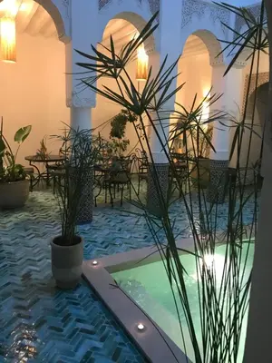a courtyard with a pool and tables and plants at Riad Dollar Des Sables & Spa in Marrakech