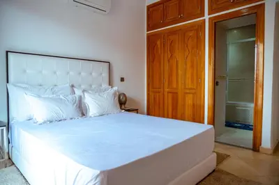 a bedroom with a white bed with a wooden door at villa 5 chambres pour famille avec piscine & parking in Marrakech