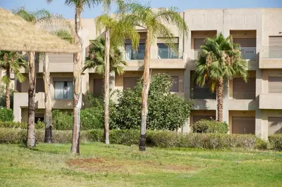 an apartment building with palm trees in front of it at Havre de Paix Piscine Lagon & parc in Marrakech