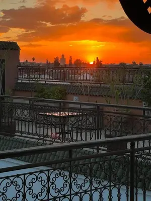 a sunset from a balcony with tables and chairs at Riad Afous in Marrakech