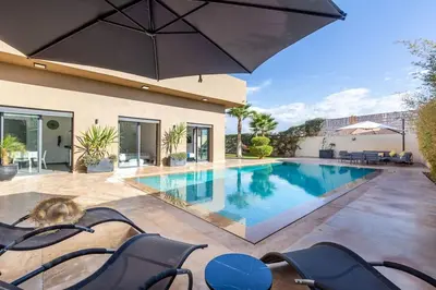a swimming pool with chairs and an umbrella at Villa Dalia, Personnels et option piscine in Marrakech