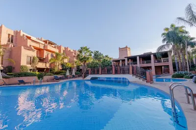 a swimming pool in a resort with palm trees and buildings at Alqantara in Marrakech