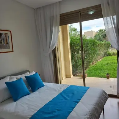 a bed with blue pillows in front of a sliding glass door at Appartement de luxe Prestigia in Marrakech
