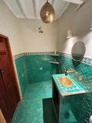 a green tiled bathroom with a sink and a mirror at Dar Kamilya in Marrakech