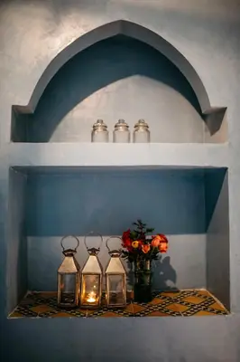 a shelf with three bottles and a vase of flowers at Riad BE Marrakech in Marrakech
