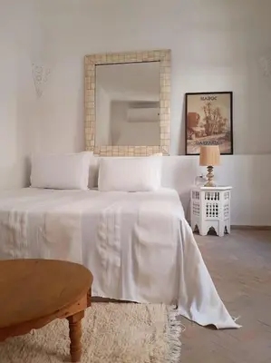 a white bedroom with a bed and a mirror at Riad Nour, Maison de charme. in Marrakech