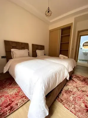 a bedroom with two beds with white sheets and a rug at App centre-ville in Marrakech