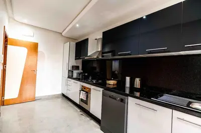 a kitchen with black cabinets and white appliances at Appartement Luxe Riad Garden Marrakech 3 piscines in Marrakech