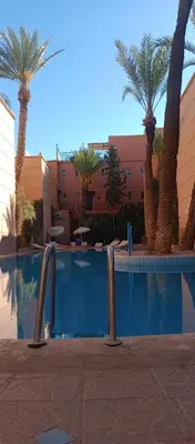 a swimming pool with palm trees in front of a building at Riad Nour Resorts in Marrakech
