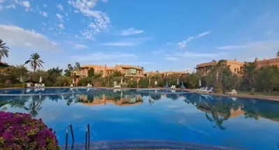 a large swimming pool in a resort with buildings in the background at Les Jardins de la palmeraie in Marrakech