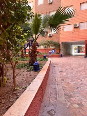 a park with two palm trees in front of a building at Charmant appartement avec piscine 2chambres au cœur de Guéliz in Marrakech