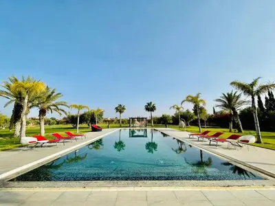 a swimming pool with red chairs and palm trees at Villa Dar El Hna in Marrakech