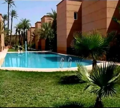 a swimming pool with palm trees in front of a building at Riad yazuinaa in Marrakech