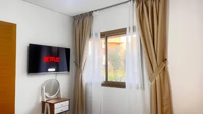 a room with a window with a tv on the wall at mini-villa situee dans une residence Prestigia à Marrakech, avec une vue sur la piscine et le golf une securite 24h sur 24 et une proximite ideale de l aeroport 5 minutes C est une offre parfaite pour des vacances in Marrakech