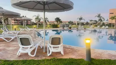 a group of chairs and an umbrella next to a pool at Appartement de Luxe avec Jardin Vue sur la Piscine Golf Securise 24h sur 24 a 5 Minutes de l Aeroport in Marrakech
