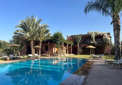 a swimming pool in front of a house with palm trees at Villa Keshmere in Marrakech