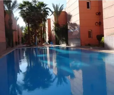 a large blue swimming pool with palm trees and buildings at Riad marrakech boujloud in Marrakech
