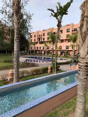 a swimming pool with palm trees and a large building at Appart Premium Village Marrakech in Marrakech