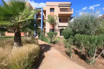 a building with a palm tree next to a dirt road at Appart-Oasis/3 Piscines/2 Terrasses in Marrakech