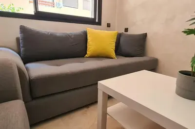 a couch with a yellow pillow in a living room at Appartement 2 chambres vue Piscine à Guèliz en face la gare de train marrakech in Marrakech