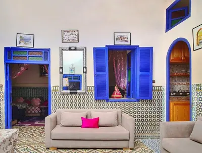 a living room with blue windows and a couch with a pink pillow at Riad Sultana - 10 min à pied de Jemaa El Fna in Marrakech