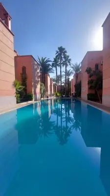 a large swimming pool with blue water and palm trees at Agréable maison familiale in Marrakech