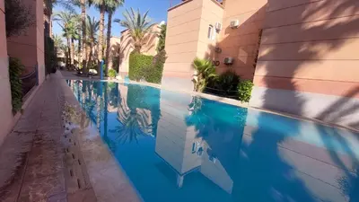 a swimming pool next to a building with palm trees at Agréable maison familiale in Marrakech