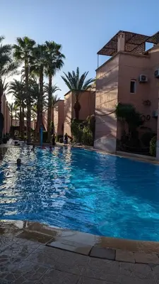 a large blue swimming pool with palm trees and a building at Riad almohafidon in Marrakech