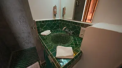 a green tiled bathroom with a sink and a mirror at Riad Anahata Marrakech in Marrakech