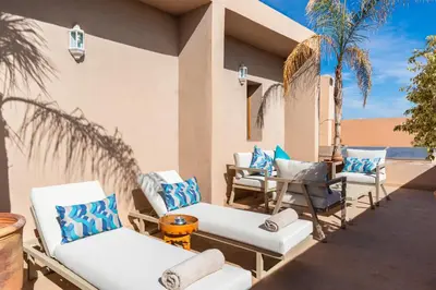 a patio with chairs and a table and palm trees at le petit dar alwalidine in Marrakech