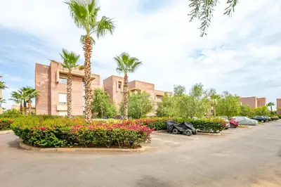a parking lot with palm trees and flowers and cars at Appartement luxe Prestige Opale Golf in Marrakech