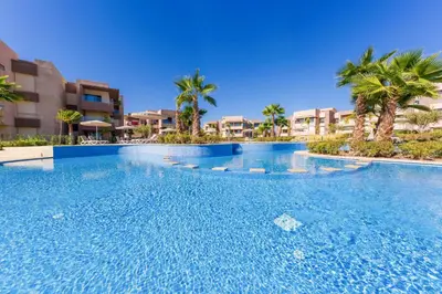 a large swimming pool with palm trees and buildings at Vue Montagnes, Golf et Piscine, Luxe à Marrakech in Marrakech
