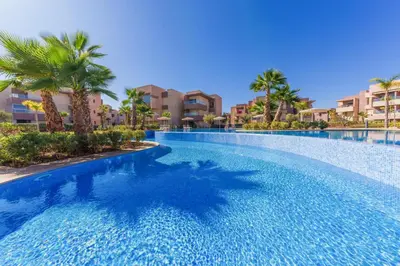 a large swimming pool with palm trees and buildings at Vue Montagnes, Golf et Piscine, Luxe à Marrakech in Marrakech